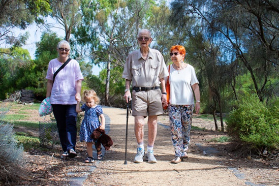 wo older women and one older man and one child walking down a dirt track surrounded by trees. The man is using a walking stick. f