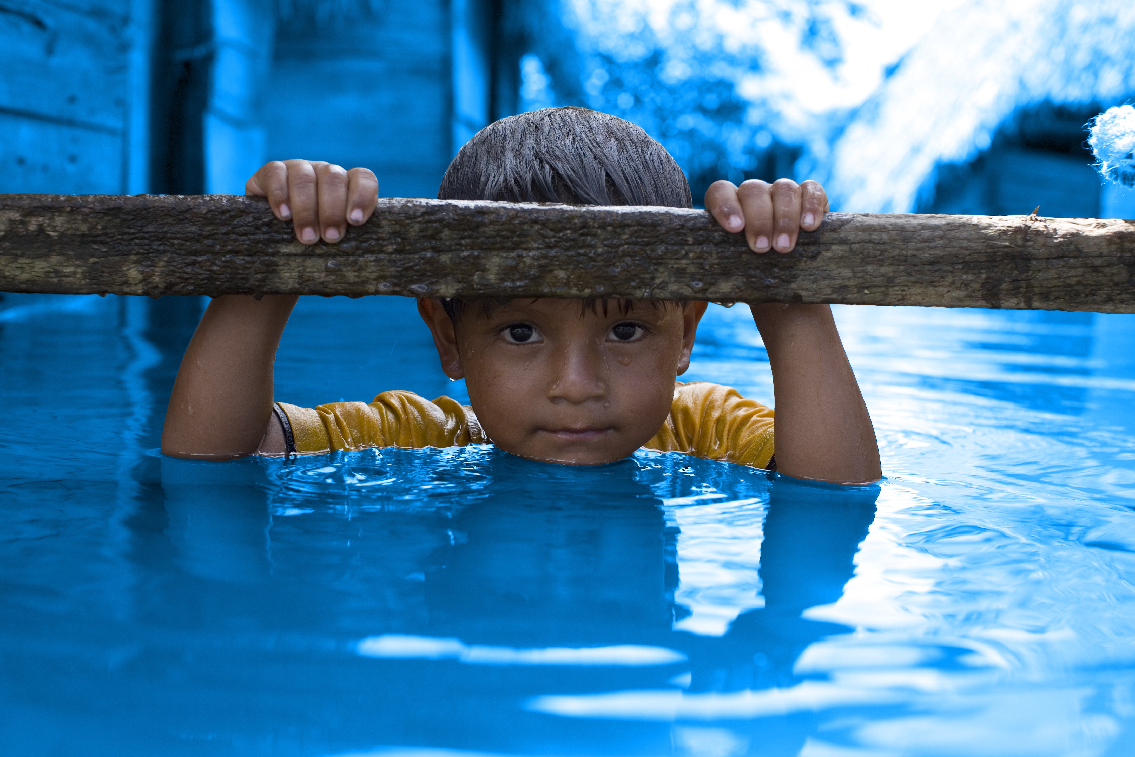 A small boy, in flood water up to his neck, holds on to a ledge outside his flooded home, in Nucleo 38 Village in the district of San Julian in Santa Cruz Department