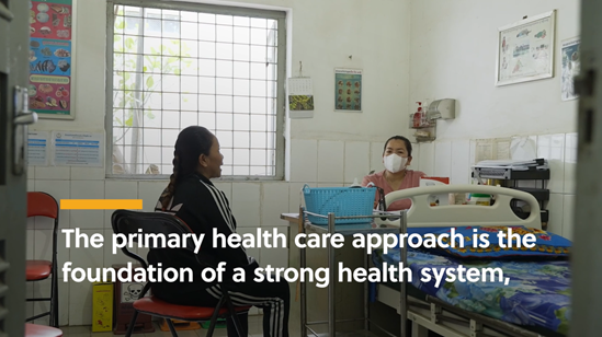 A woman is inside a health centre and is talking to a health worker who is wearing a mask. Text says the primary health care approach is the foundation of a strong health system.