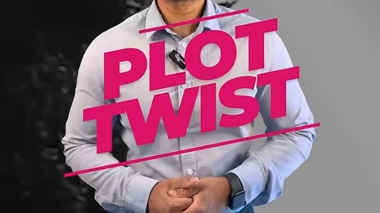 A smiling man standing up and looking into the camera, with the overlay text "plot twist" in bold dark pink letters.