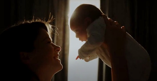 A mother is holding her baby up in front of her, locking eye contact and smiling.