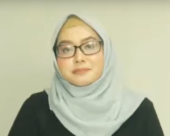 A video snapshot of a woman wearing a veil and glasses, looking into the camera.