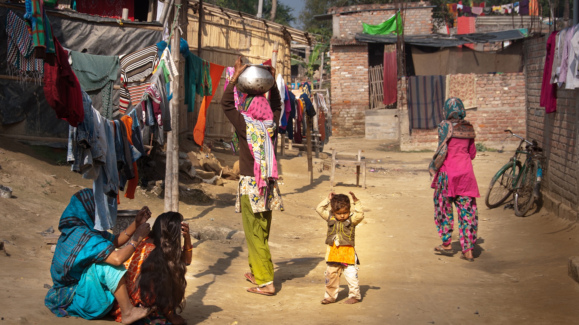 Photo 1 Photo of people walking and sitting on a dirt road between homes in Darbhanga, India.