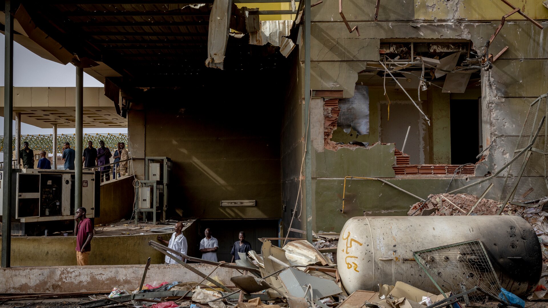 Healthcare workers emerge from the basement of a damaged hospital building with big holes in the wall and roof. In front there is a pile of rubble..