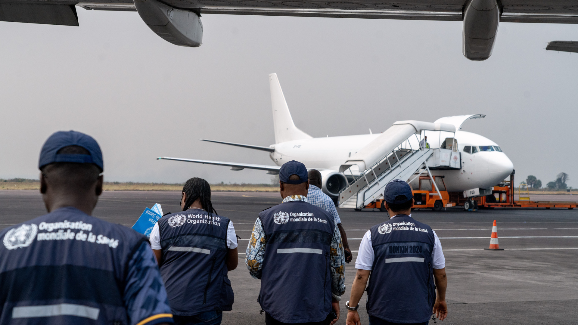 People in WHO vests walk to meet a plane on the tarmac