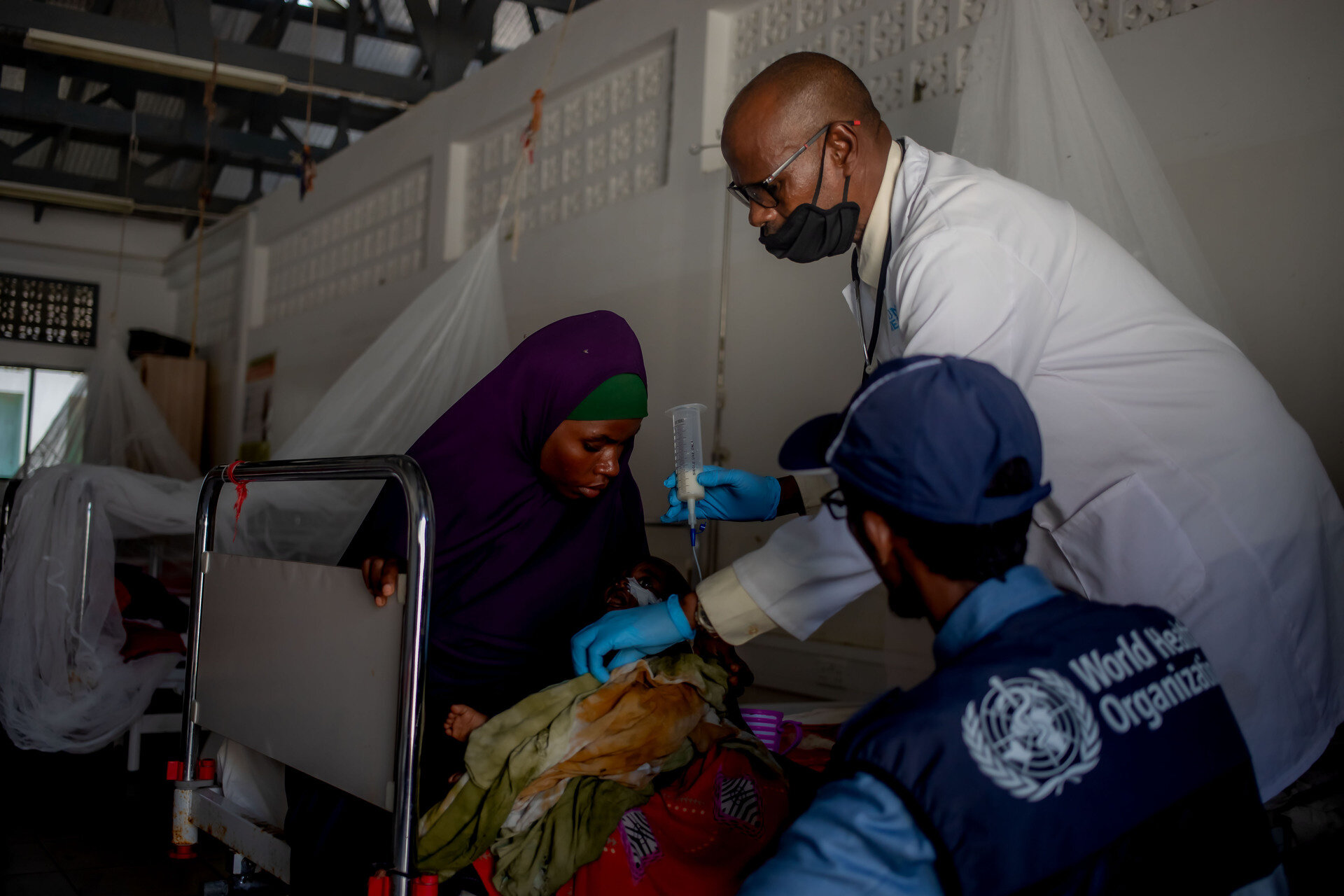 WHO staff and doctor treat child in mother's arms for severe acute malnutrition
