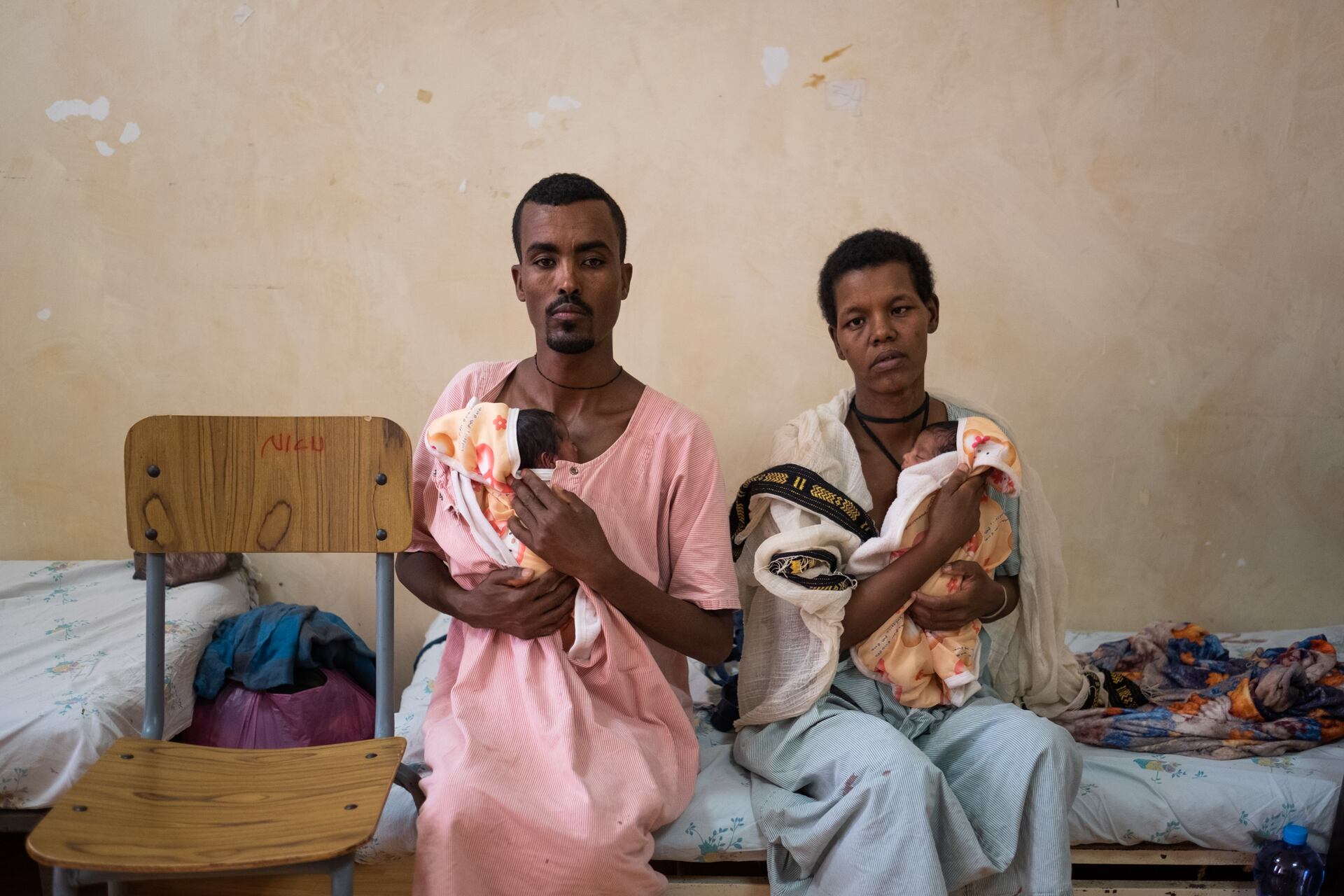 Ethiopian parents sitting on a bed, each provide skin-to-skin care to their preterm twins