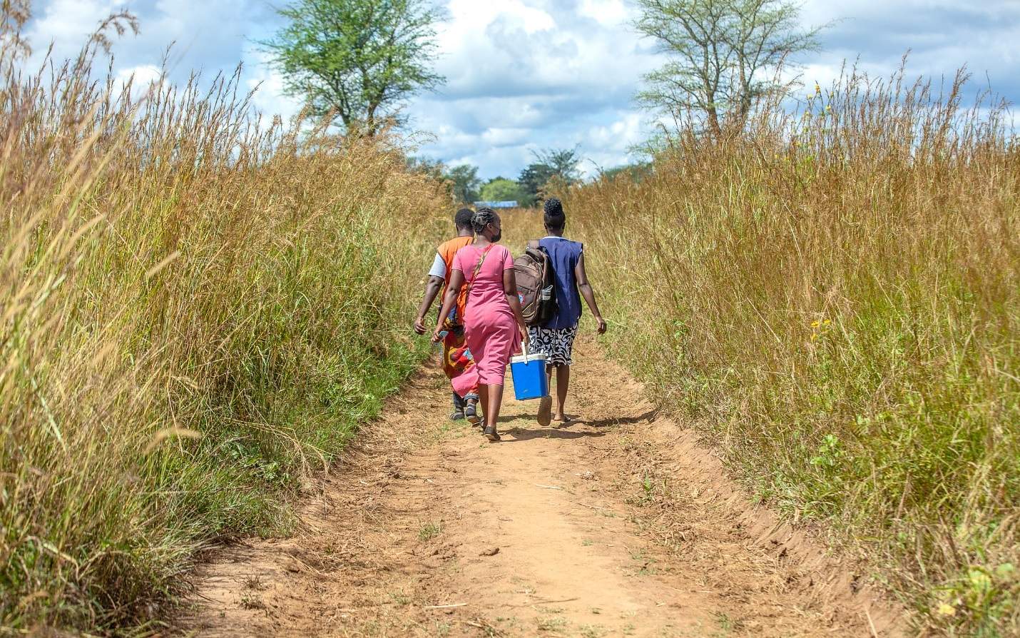 Three women walking on a dirt road seen from behind.