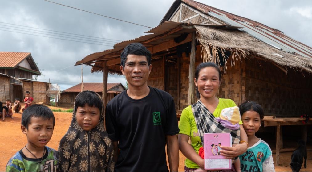 A couple and their four children are standing in front of their house