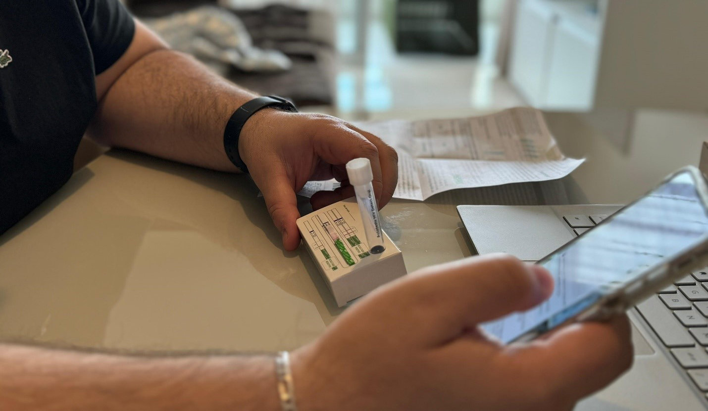 Close up of hands of holding a smartphone and a HIV self-test kit.