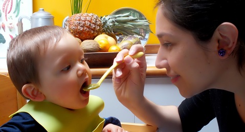 A woman is feeding a baby with a spoon