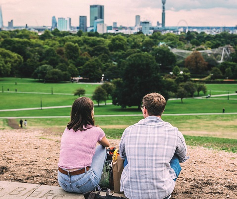 Two boys leaning against a wall, gazing at a city and its lush green surroundings.