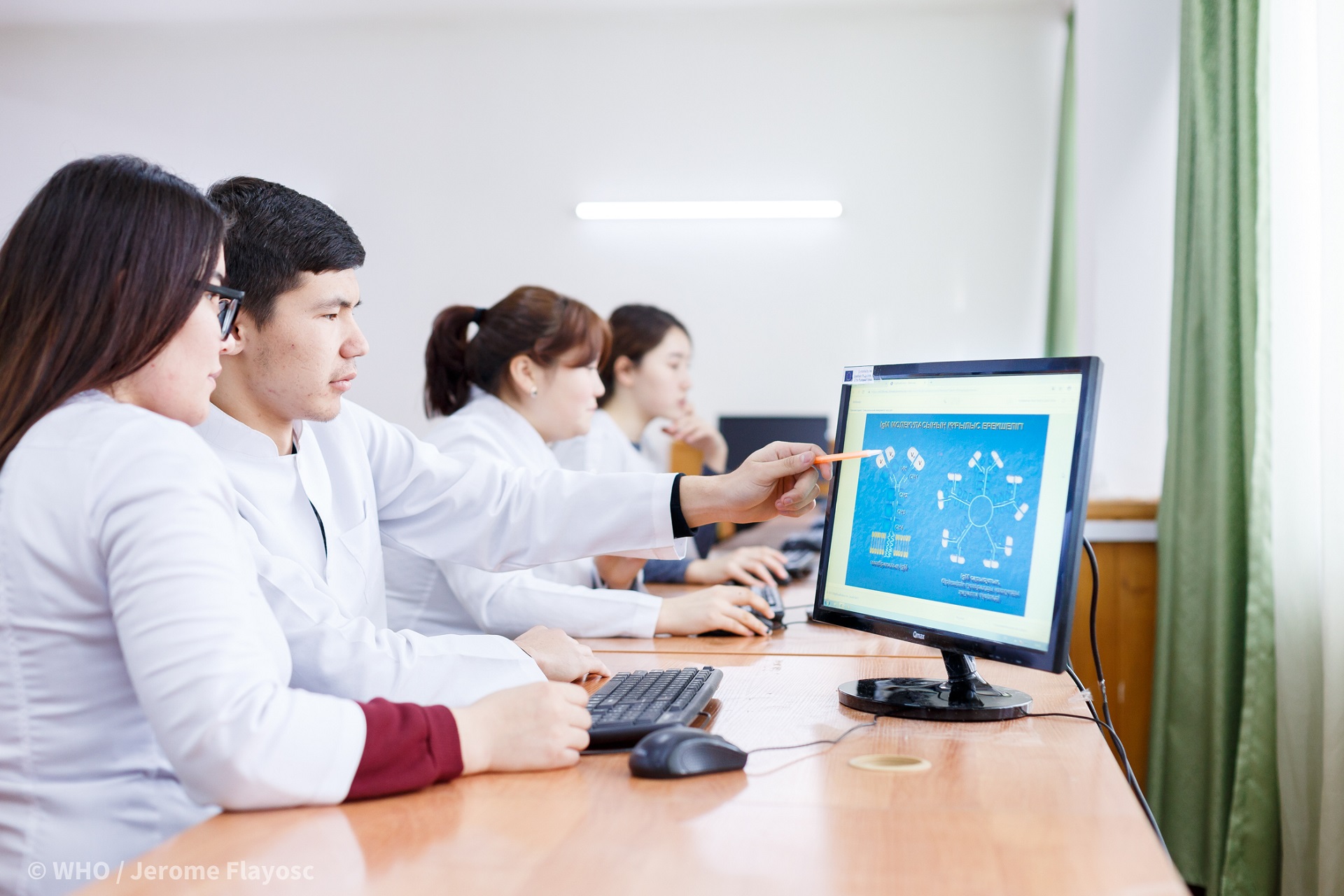 Students in white coats in front of computer screen