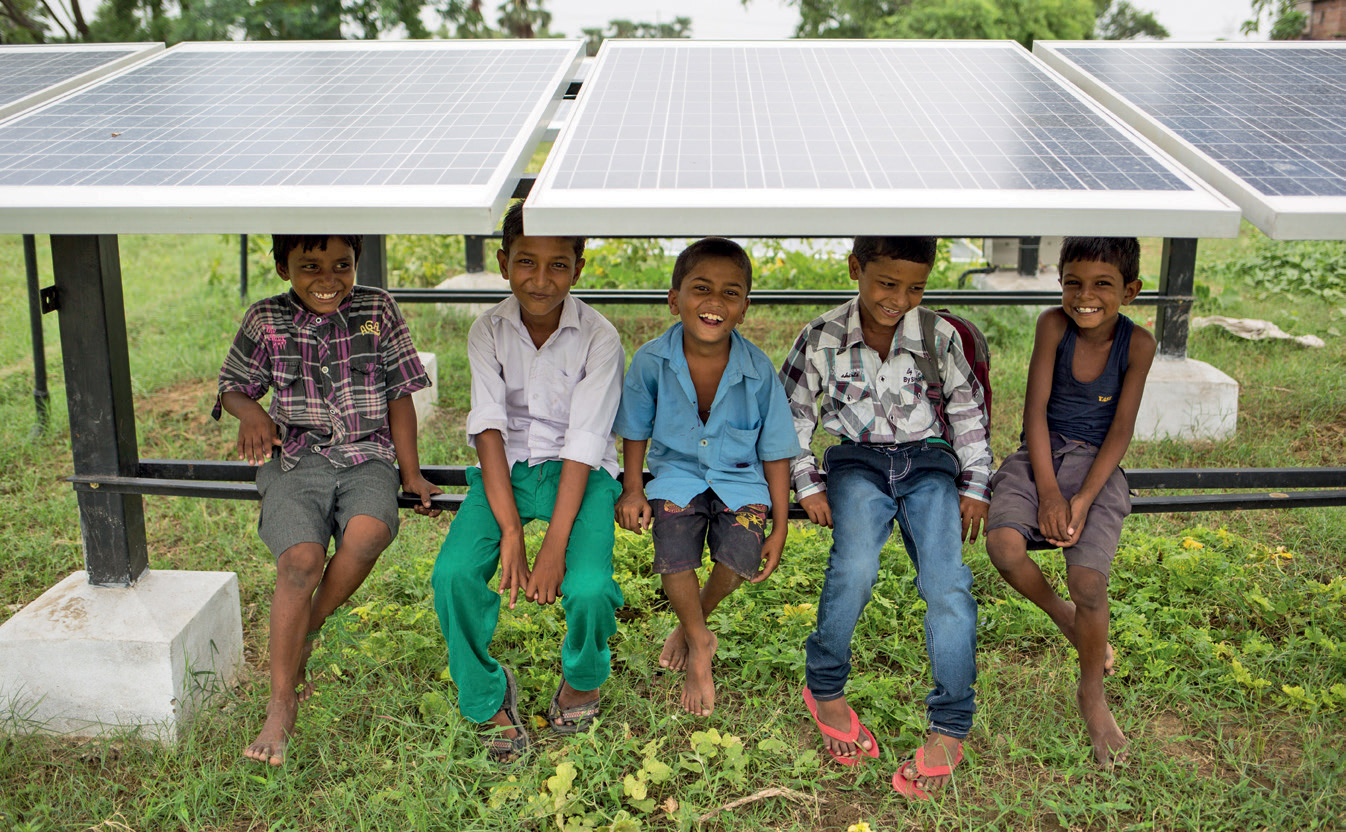 Five smiling children sitting under a solar panel. 