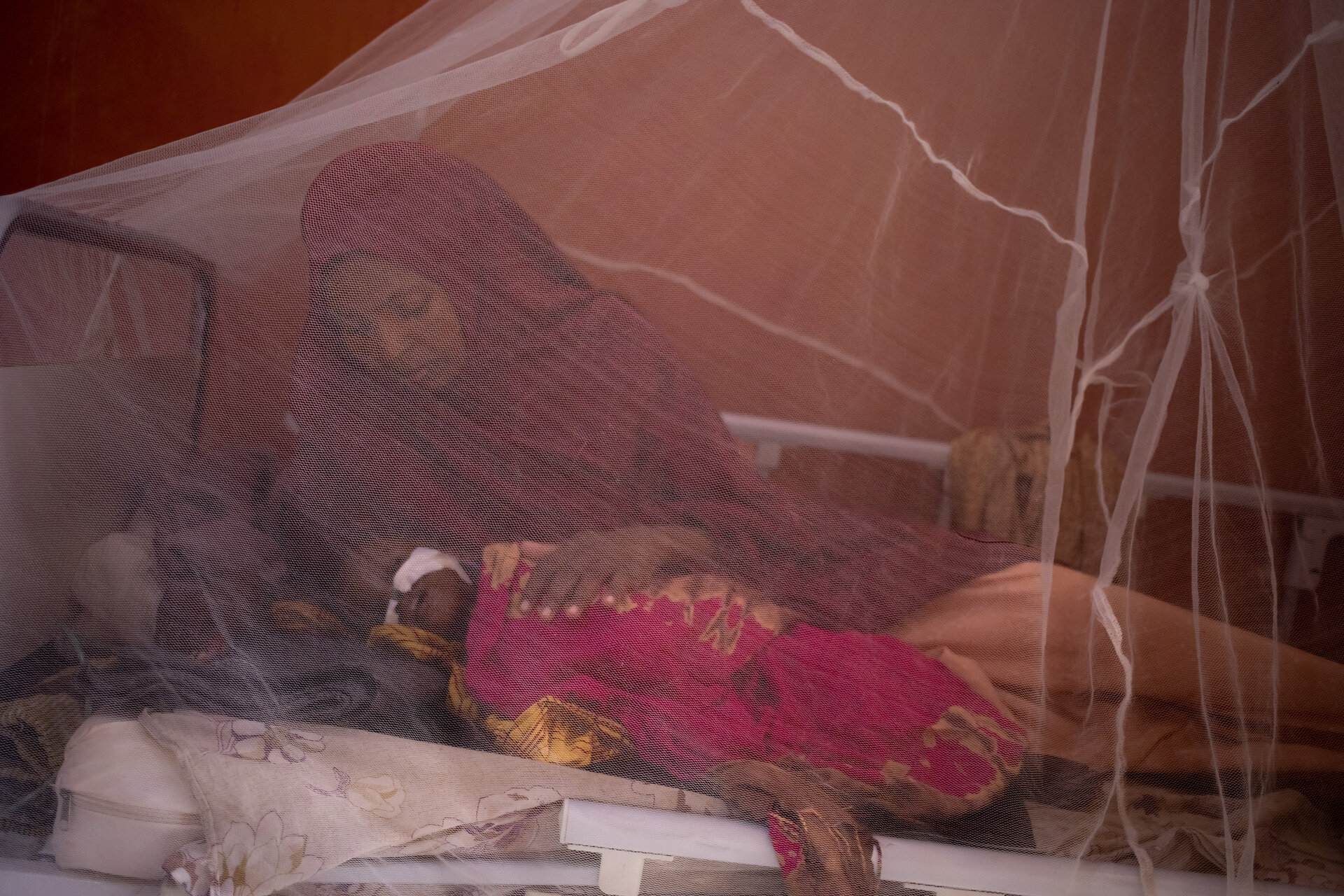 mother holds her malnourished baby protected by a malaria net