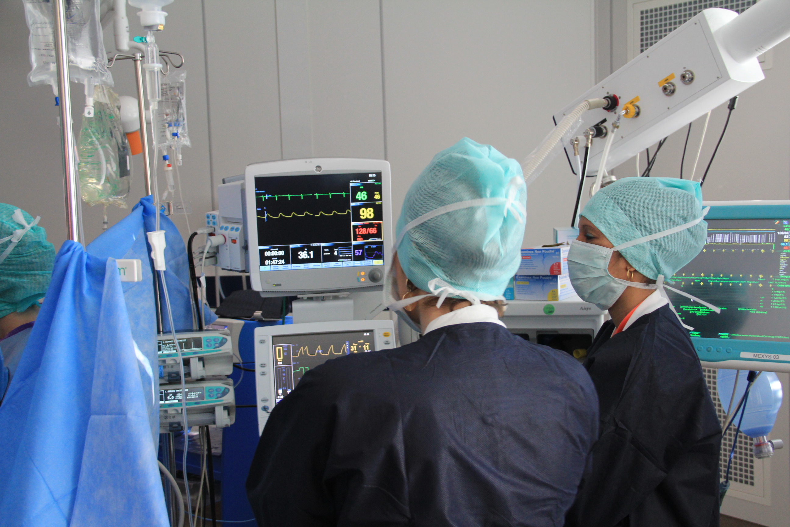 Two nurses standing in front medical equipment in the operating room during surgery.