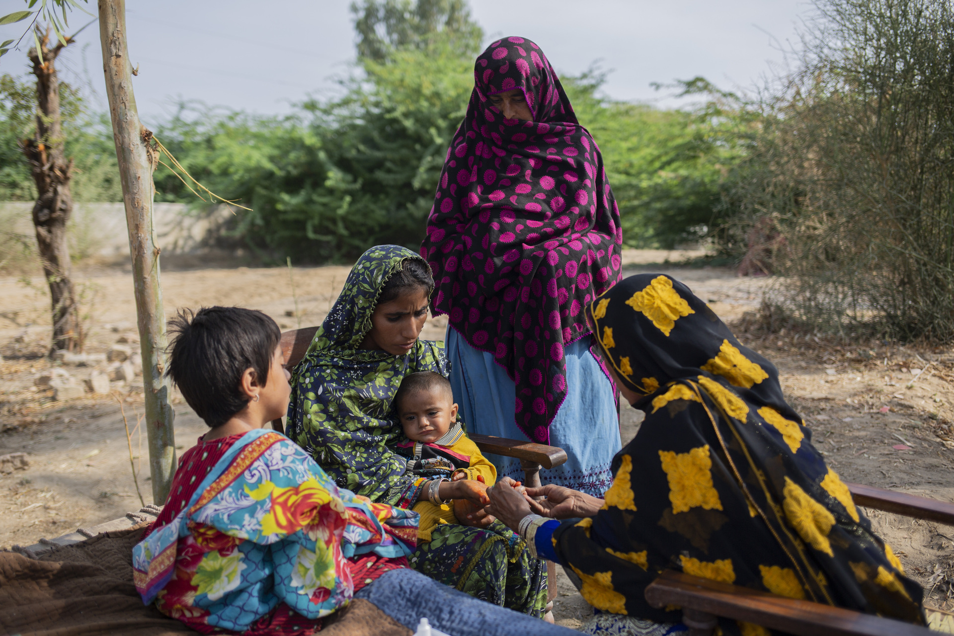 3 female adults and 2 children in a refugee camp sitting in the open air