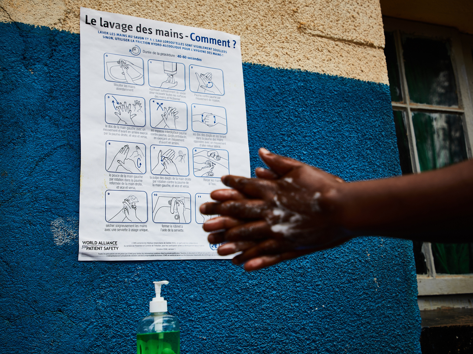 Person washing hands with instructional poster in the background