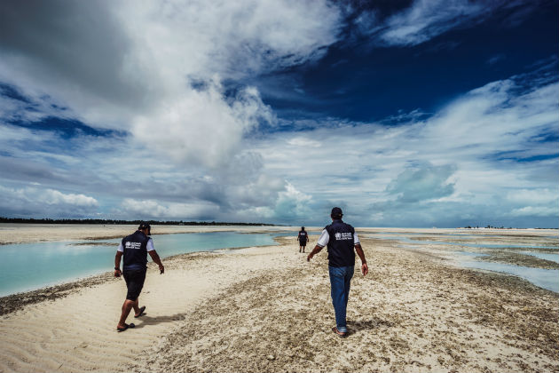 People in WHO vests walk across an empty beach.
