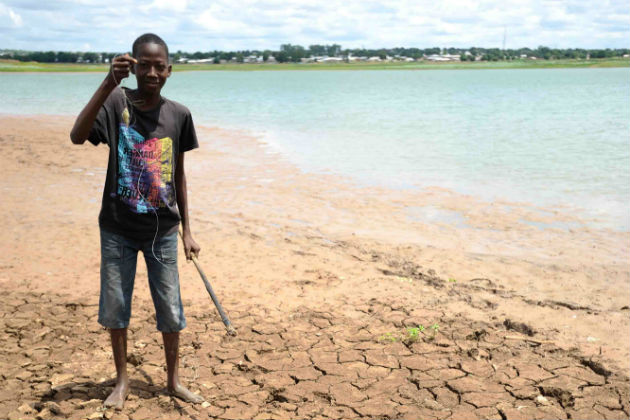 A man stands on a beach with clay that is dried up and cracked, showing the effects of el nino.