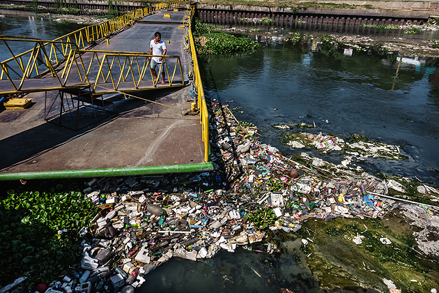 A man with an umbrella climbs on a bridge over a polluted river in the Philippines