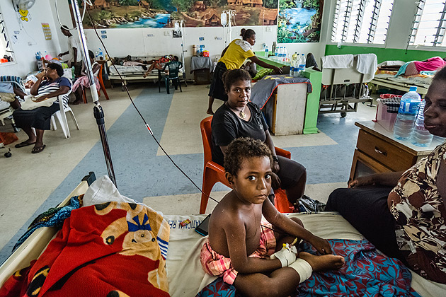 A child with his mother, sitting on hospital bed among other patients in Solomon Islands
