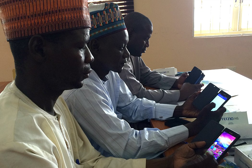 Three men working on their phones during a Local Government Area facilitator training conducted by WHO, Borno State, Nigeria 2016.