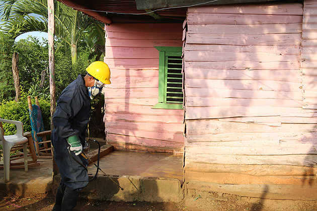 A man with mask, goggles and spraying device around a house in the Dominican Republic