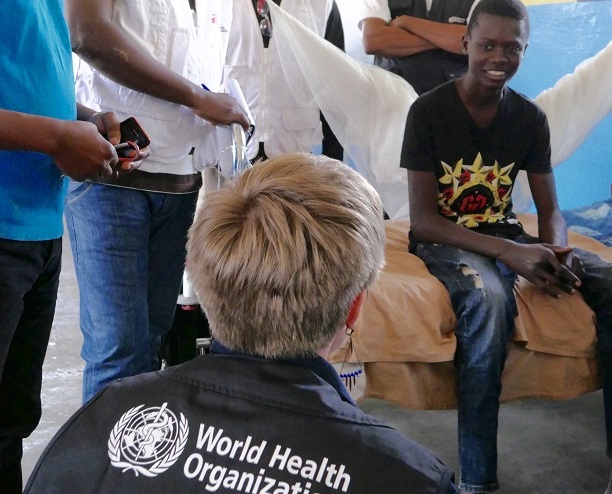 Woman wearing a WHO vest talks to a young boy who has yellow fever.