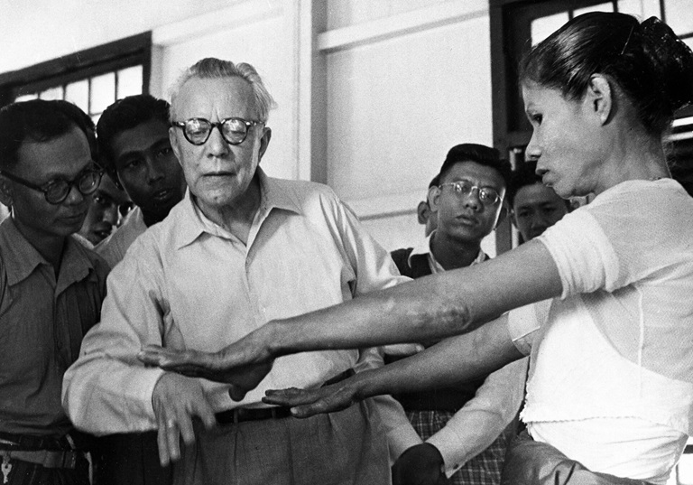 a health worker and others examine a patient's outstretched arms