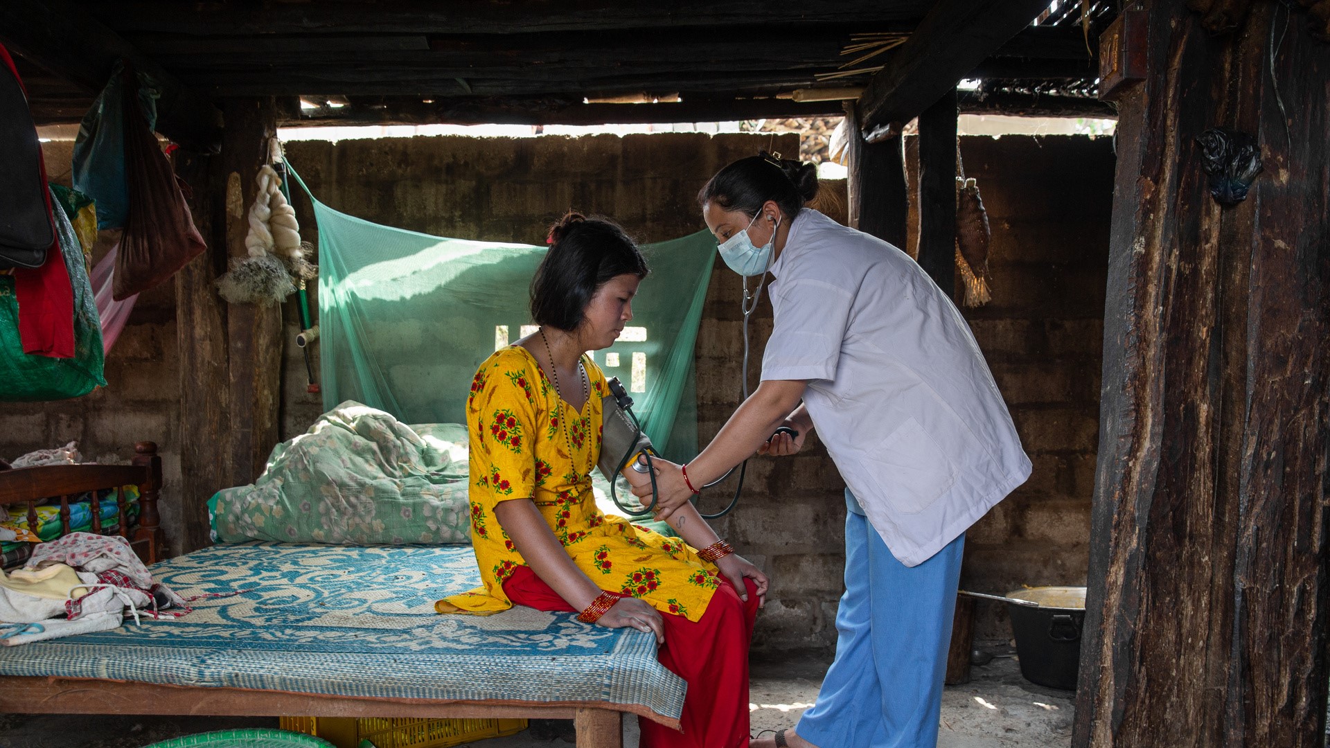 a patient sitting on a bed while a health worker performs a blood pressure measurement