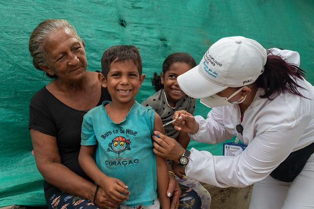 A boy is receiving a vaccine shot in the arm by a health worker.