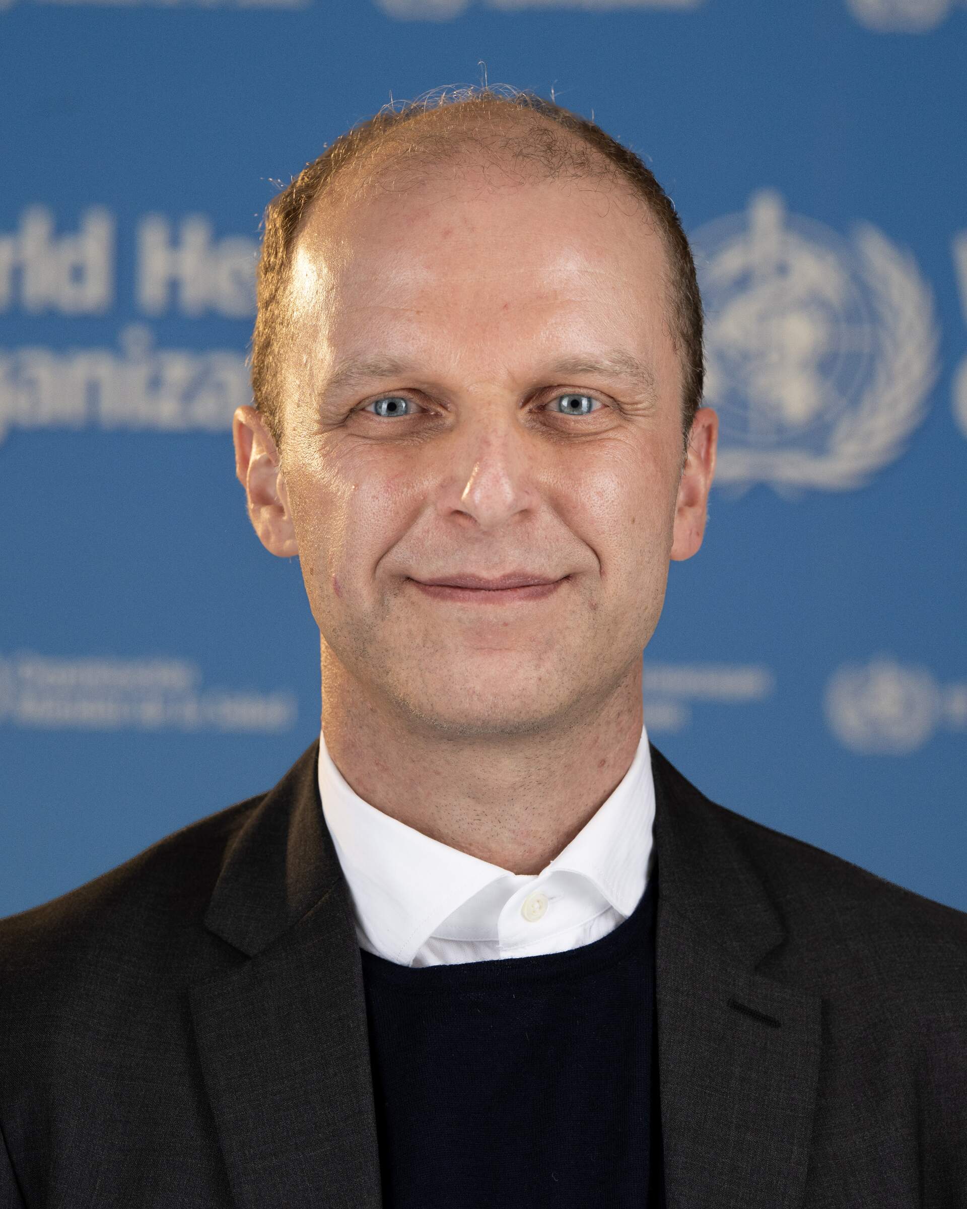 Portrait photo of a man against a WHO backdrop.