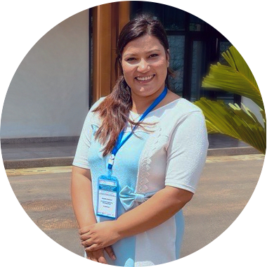 Picture of a woman standing in a street, smiling towards the camera.
