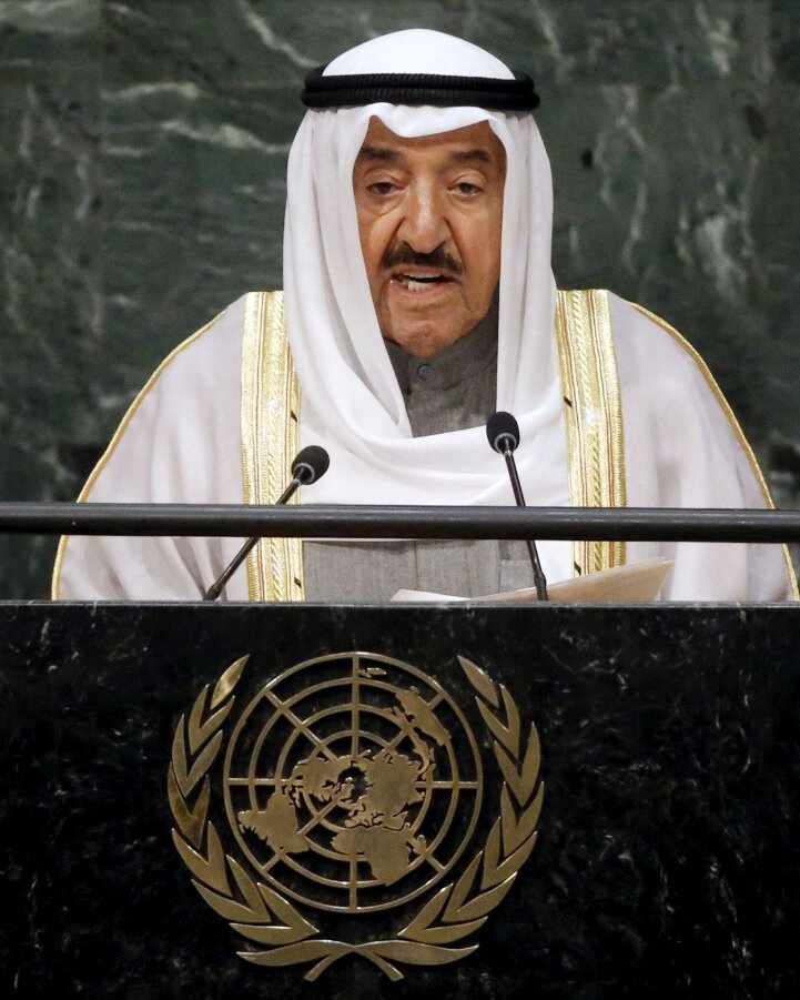 A man dressed in a ghutra and bisht, speaking from a podium with the United Nations emblem.