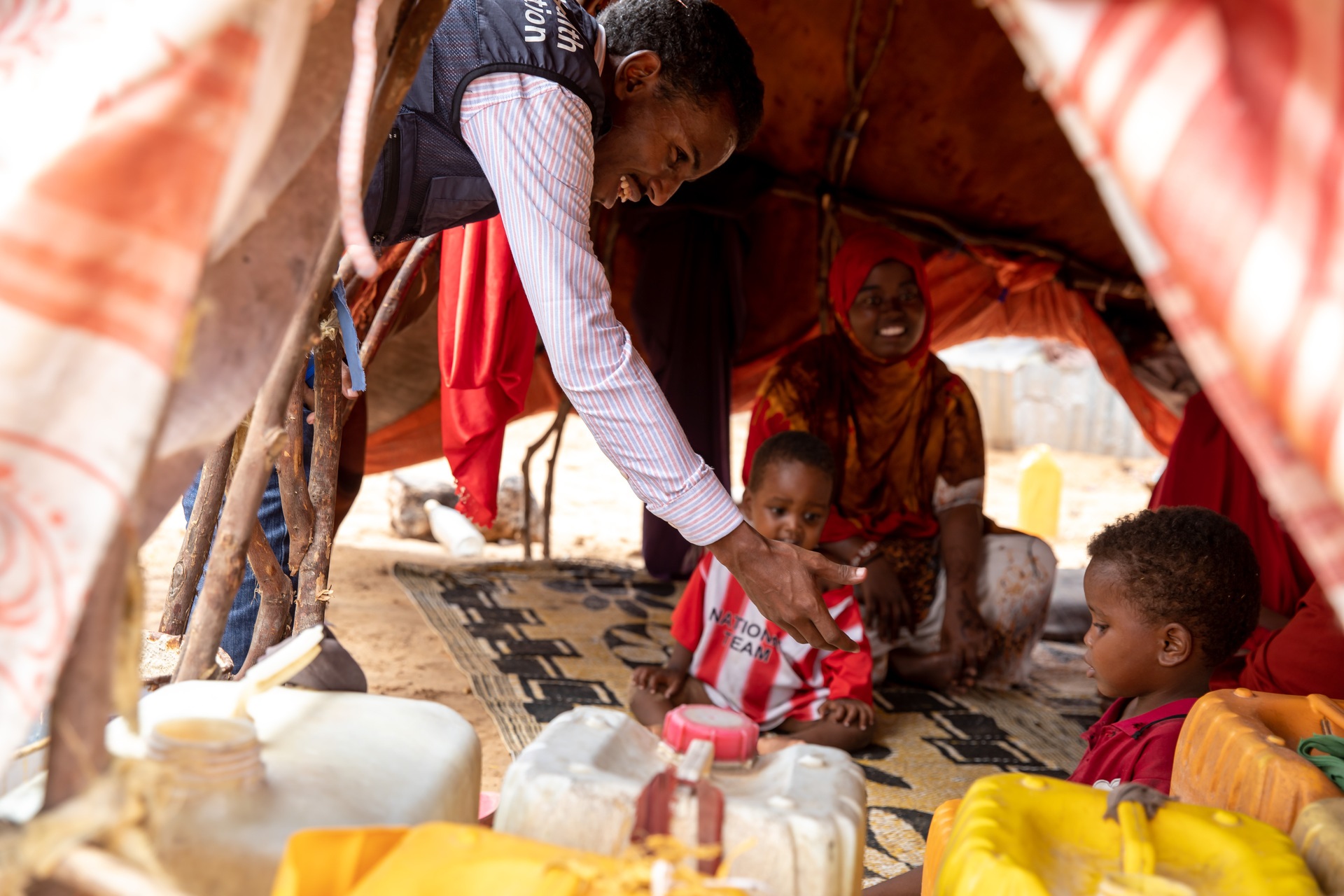 WHE 2025 Appeal Impact in 2024 Somalia A mother and two children in their camp being attended to by a health worker wearing a WHO jacket.