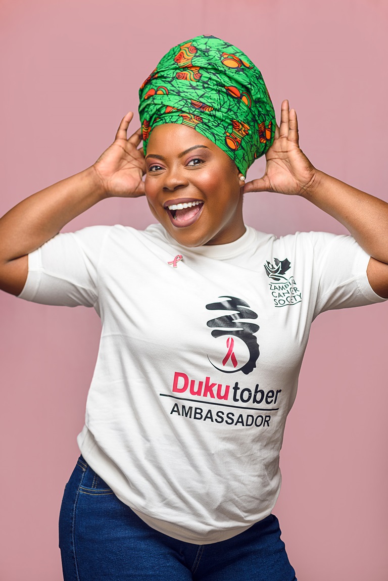 A pink social media tile with a photo of a woman wearing a Zambian Cancer Society t-shirt.