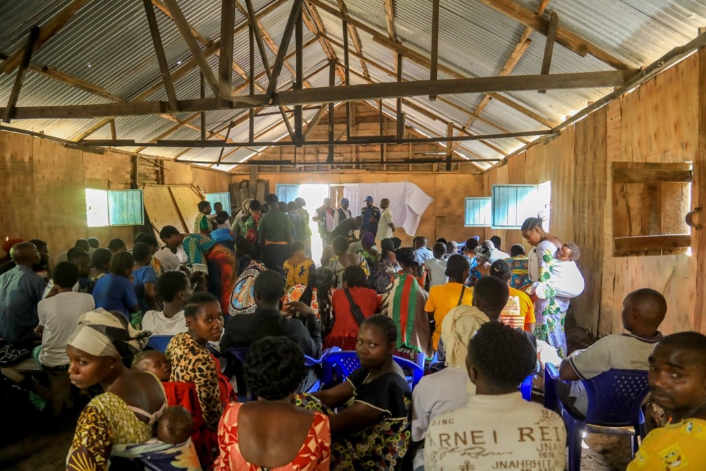 A crowd of people listens to health workers