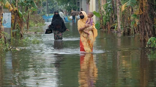 Women walking through the water with their children and belongings.