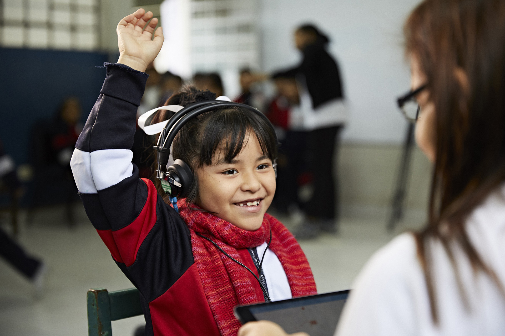 A child wearing headphones raising her hand facing a health worker