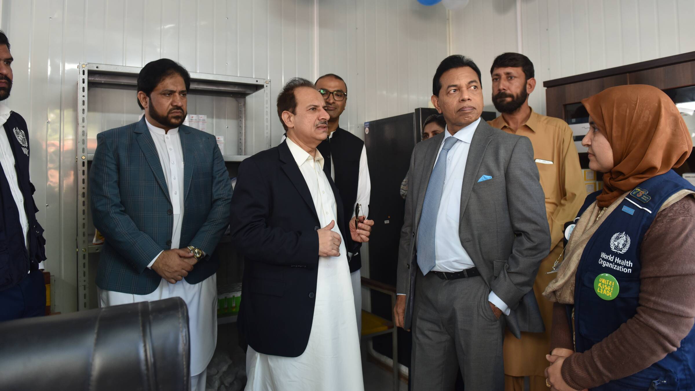 Inauguration MNCH Centre Tangi Pakistan Two WHO officers together with men in suits standing in a room.