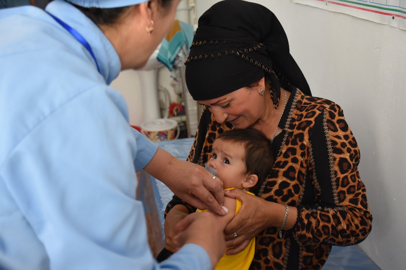 A nurse administers a vaccine to a small child sitting on his grandmothers' lap.