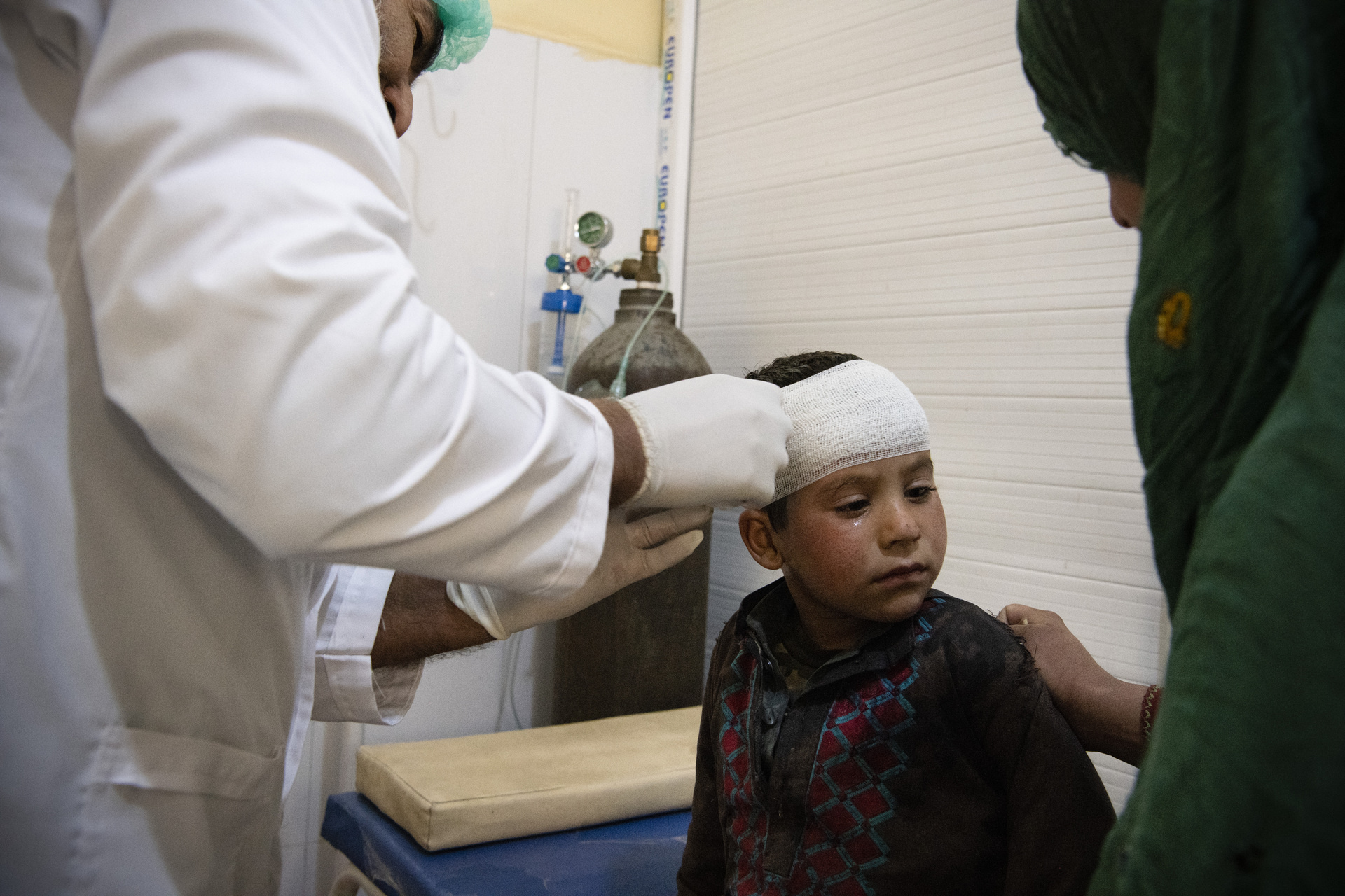 A doctor treats a child with a head injury. His mother is next to him.