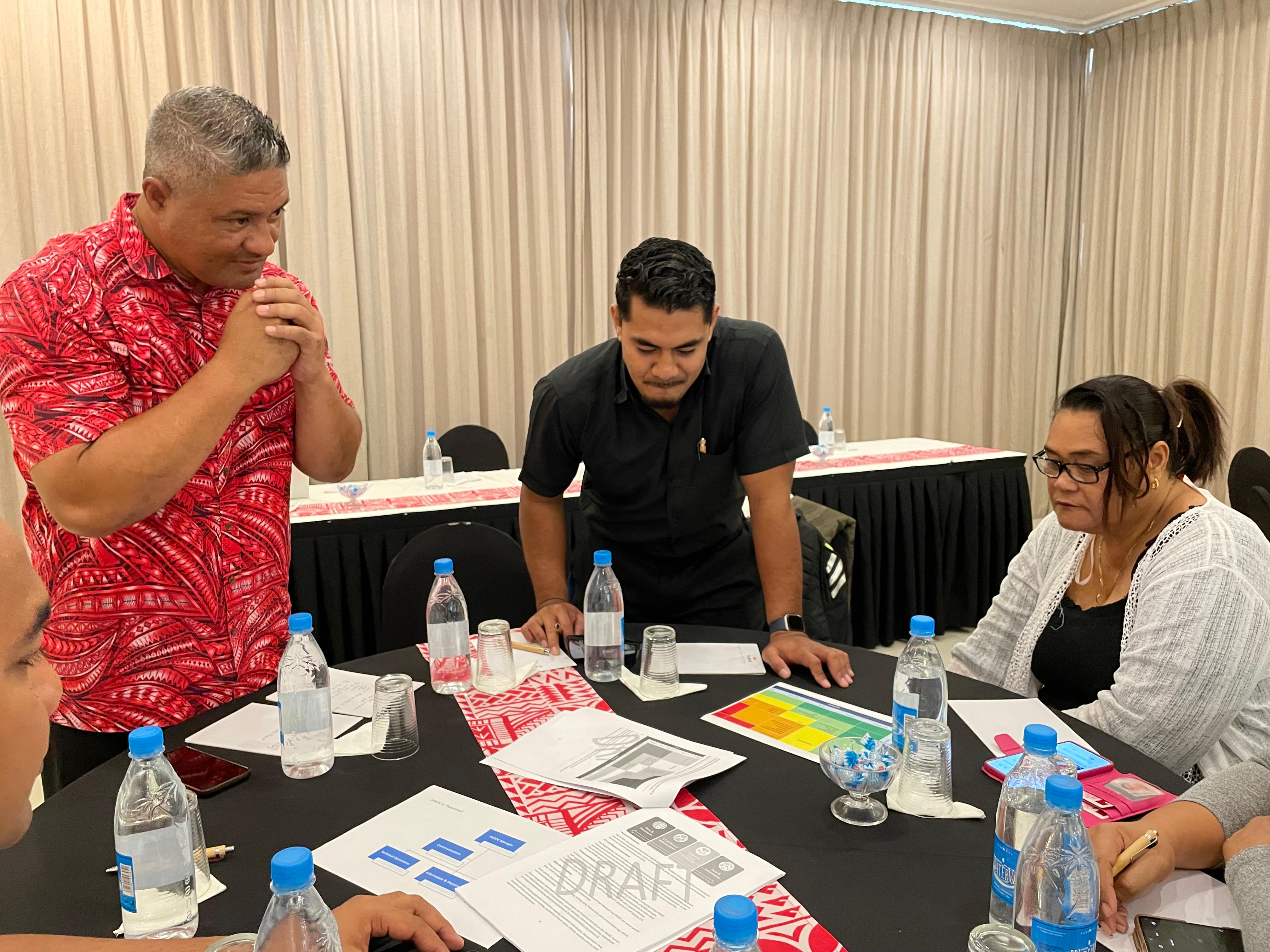 Three people looking at flow charts and information around a table