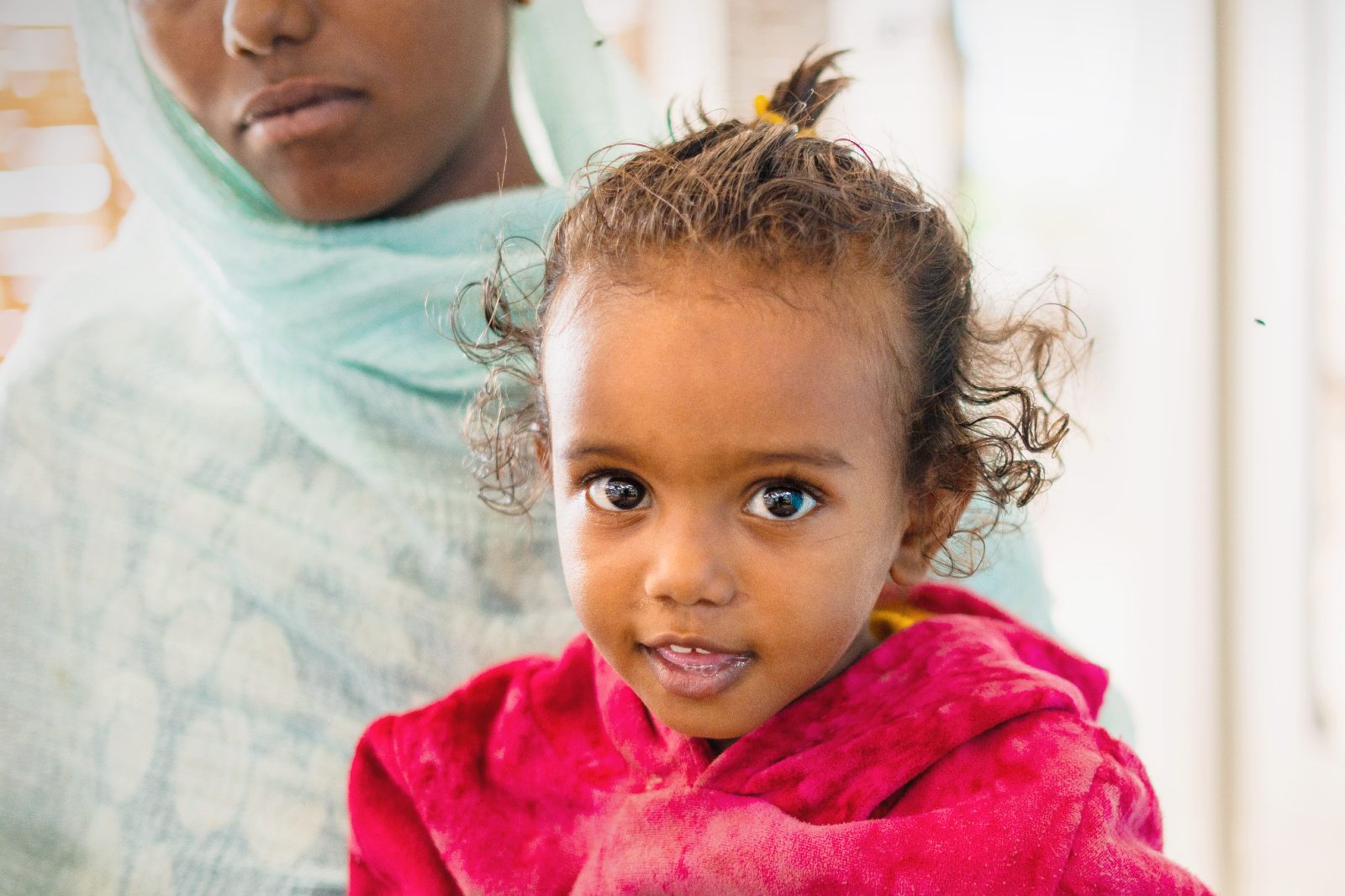Little girl sitting in her mothers lap looking into the camera.