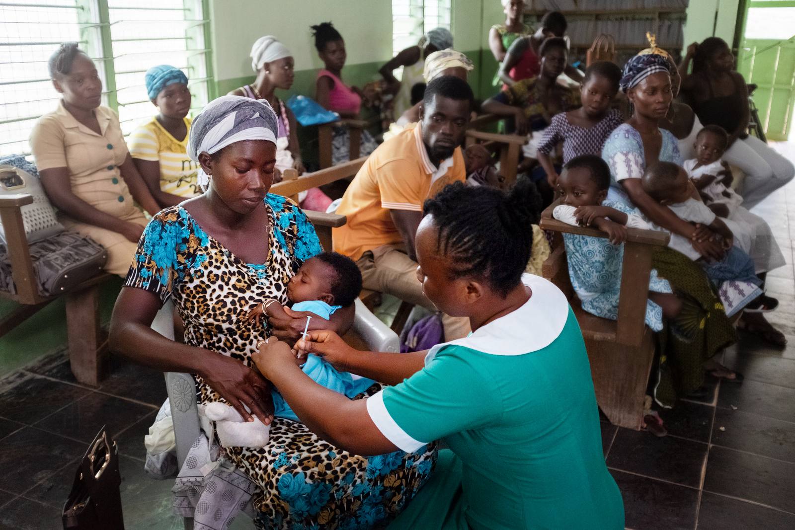 A baby laying in her mother's lap is given vaccine by a nurse in a healthcare facility.