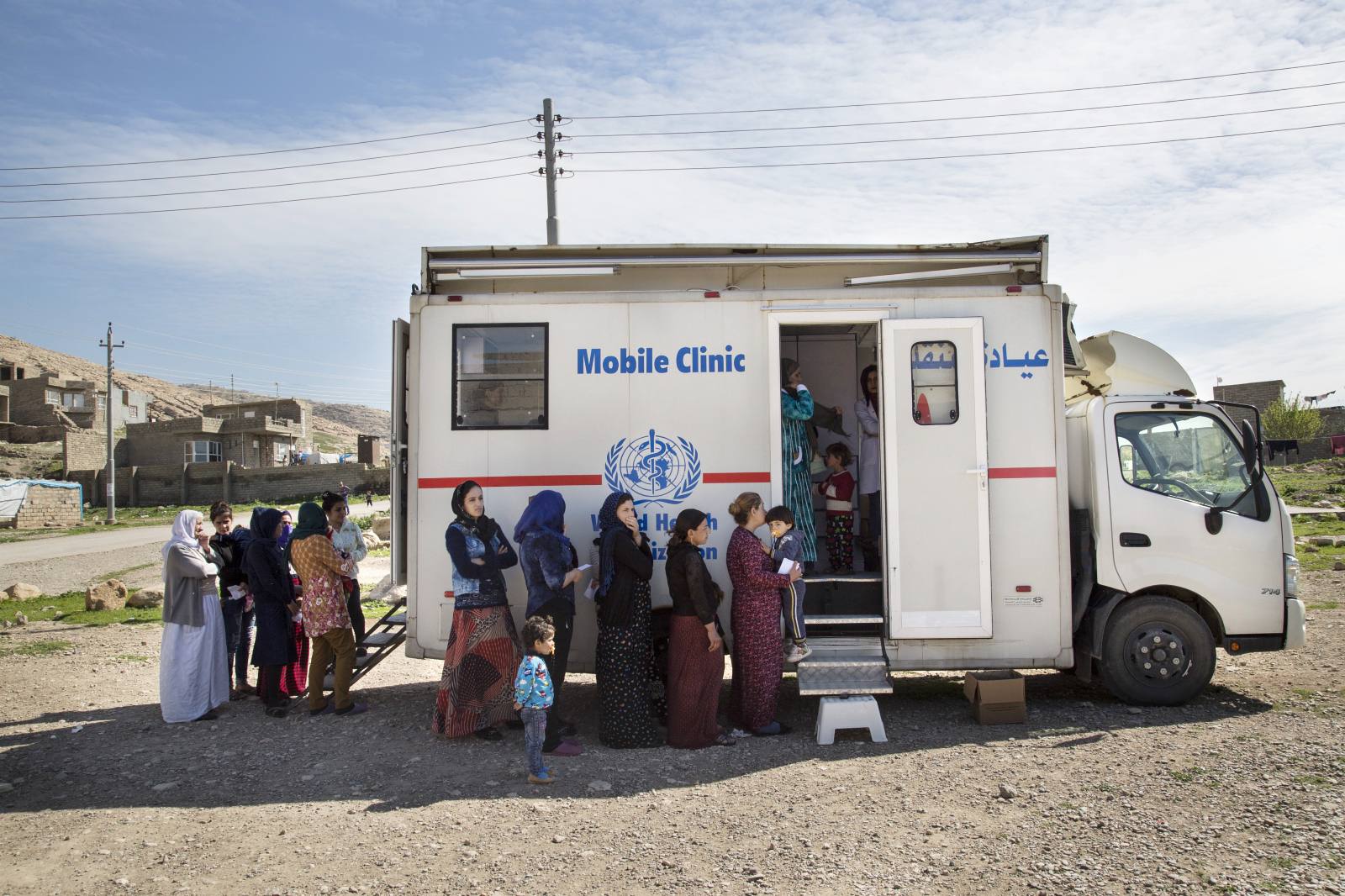 Yezidi men, women and children line up at a Mobile Clinic to get medical attention.