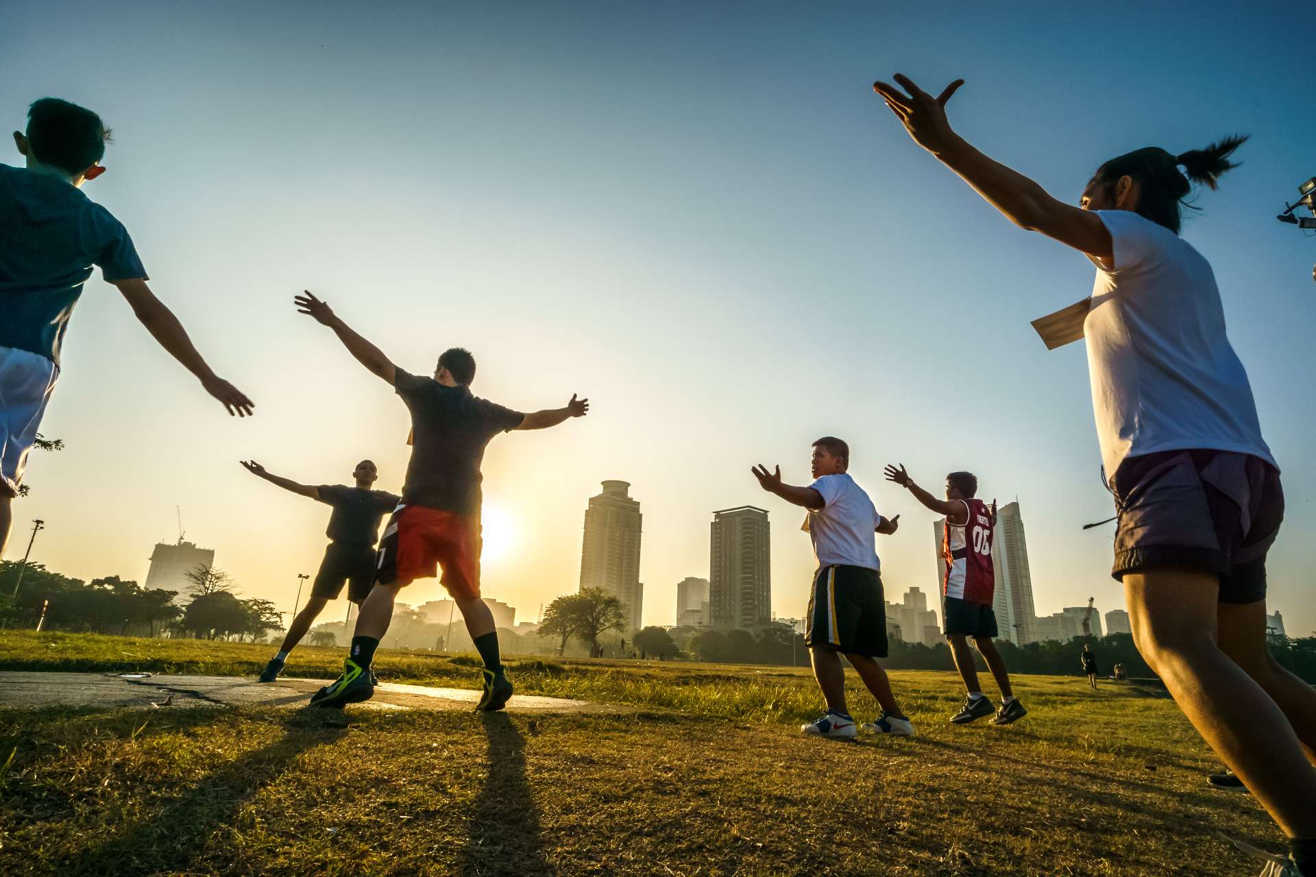 Silhouettes of people conducting morning exercises in a city park during the sunrise.