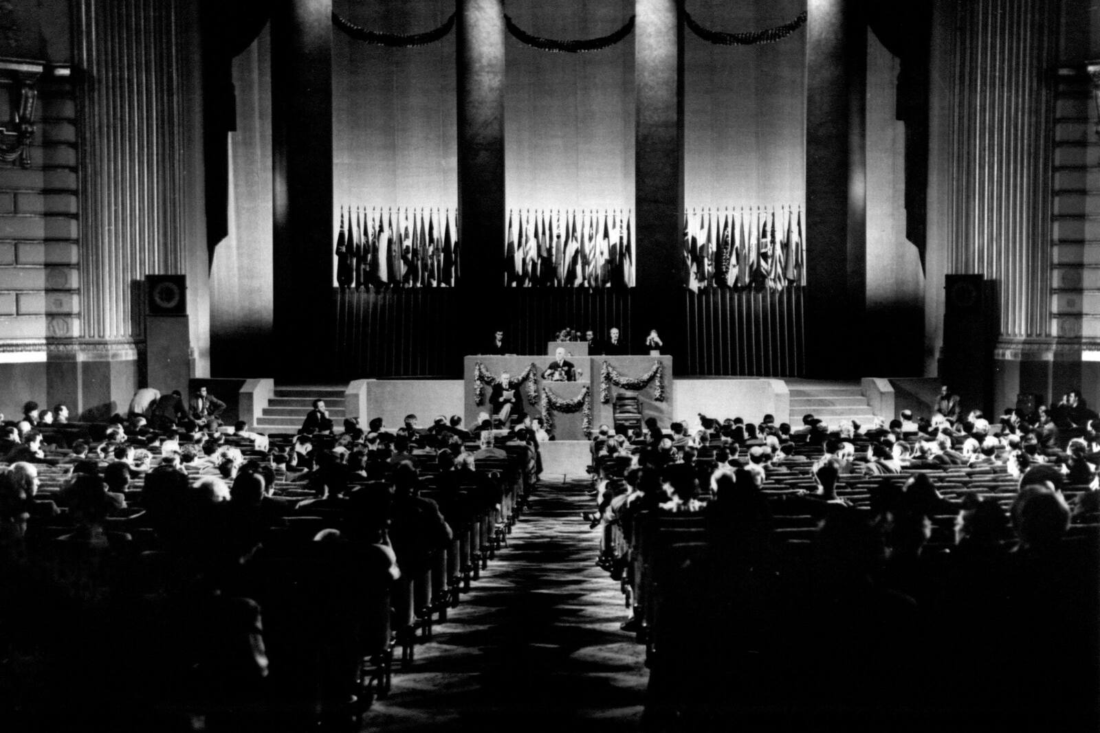 General view of a meeting of the United Nations Conference with the speaker at a podium and rows of participants listening.
