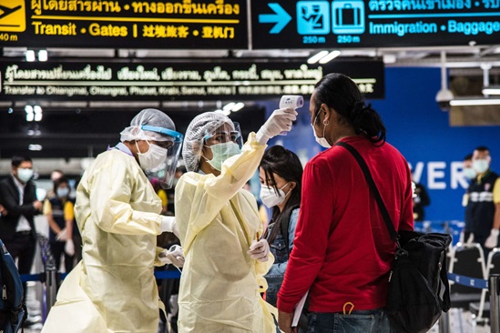 Thailand 2020: health workers dressed in personal protective equipment take the temperature of an incoming passenger in Bangkok airport's health control area